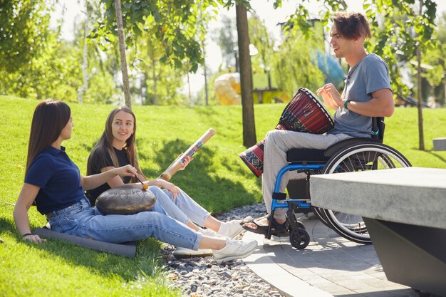 Glücklicher behinderter Mann auf einem Rollstuhl, der Zeit mit Freunden verbringt, die Live-Instrumentalmusik im Freien spielen.