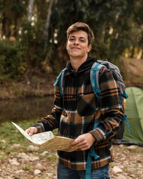 Glücklicher Campingmann im Wald, der die Karte hält