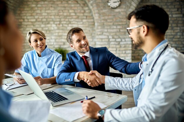 Glücklicher Finanzberater und männlicher Arzt beim Händeschütteln nach erfolgreichem Treffen im Büro