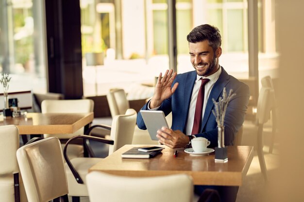 Glücklicher Geschäftsmann, der in einem Café einen Videoanruf über das Touchpad tätigt