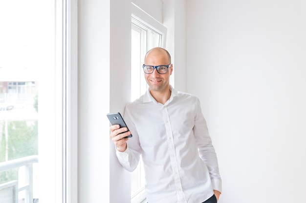 Glücklicher Geschäftsmann, der Mobiltelefon im Büro hält