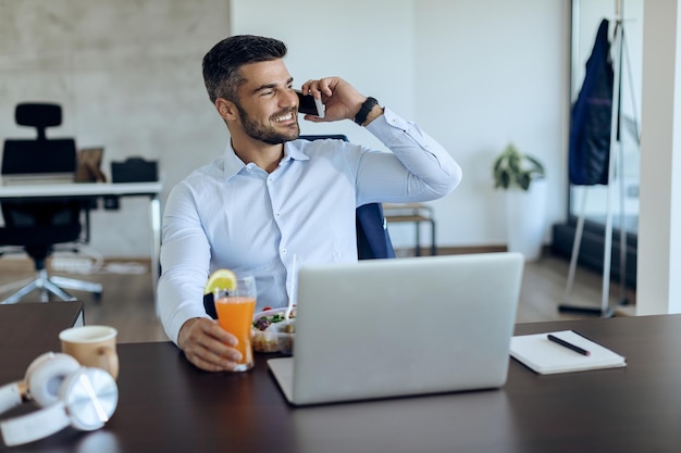 Glücklicher Geschäftsmann, der über Handy kommuniziert, während er Mittagspause im Büro hat