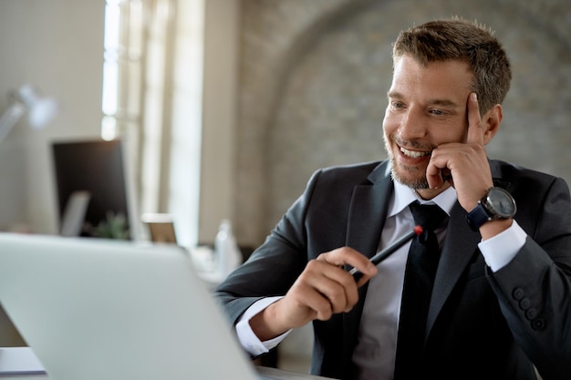 Glücklicher Geschäftsmann mittleren Alters, der an einem Computer arbeitet und eine E-Mail im Büro liest