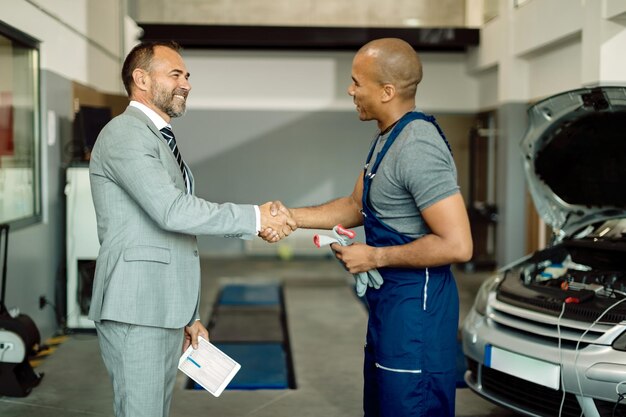 Glücklicher Geschäftsmann und afroamerikanischer Mechaniker beim Händeschütteln in der Autowerkstatt