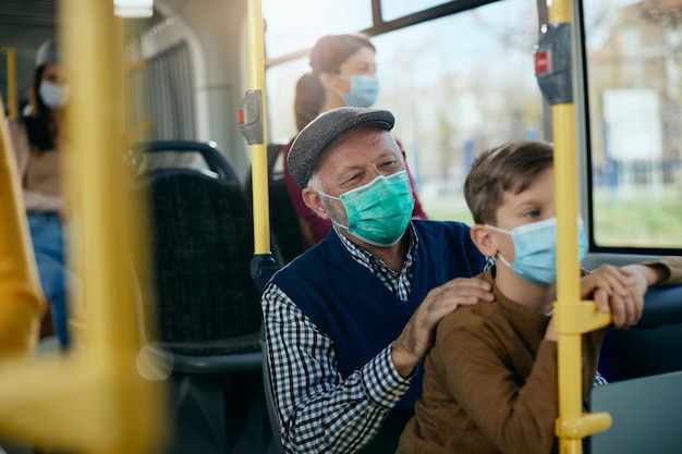 Glücklicher Großvater mit Enkel, der während der COVID19-Pandemie mit dem Bus pendelt