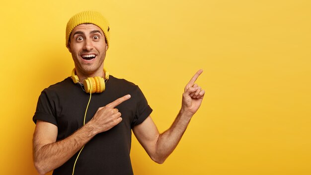 Glücklicher Hipster-Typ zeigt mit beiden Vorderfingern zur Seite und wirbt für Kopierfläche für Ihre Werbeinhalte