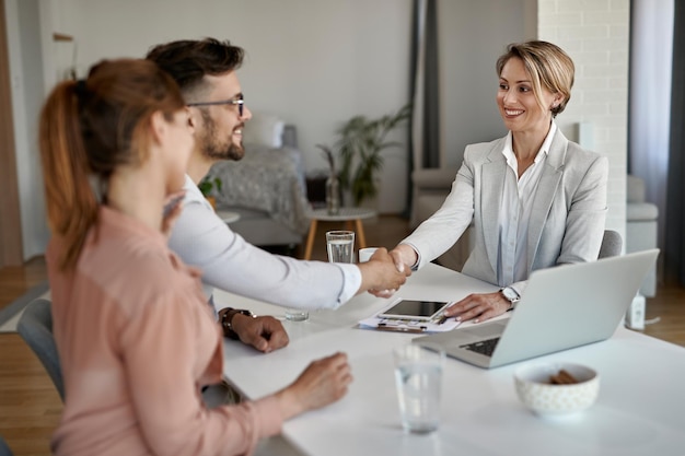 Glücklicher Immobilienmakler, der einem Paar bei einem Meeting im Büro die Hand schüttelt