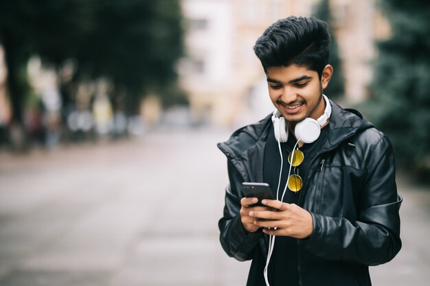 Glücklicher indischer Mann, der geht und ein Smartphone verwendet, um Musik mit Kopfhörern zu hören