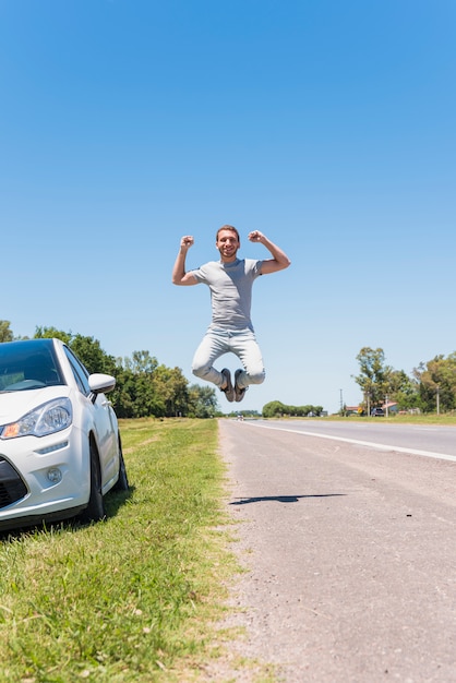 Kostenloses Foto glücklicher junge, der auf die straße nahe bei auto springt