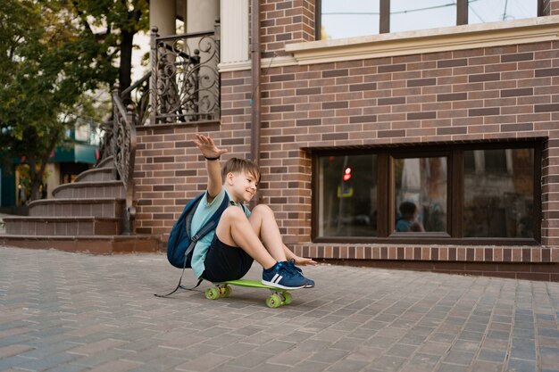 Glücklicher Junge, der auf Skateboard in der Stadt spielt, kaukasisches Kind, das Penny Board reitet