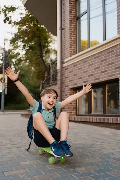 Glücklicher Junge, der auf Skateboard in der Stadt spielt, kaukasisches Kind, das Penny Board reitet