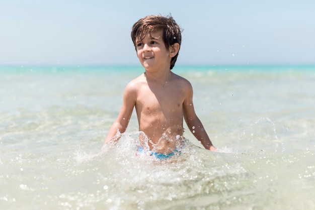 Glücklicher Junge, der im Wasser an der Küste spielt