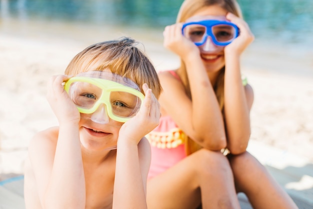 Kostenloses Foto glücklicher junge und lächelnde frau in den schutzbrillen, die auf sandufer sitzen