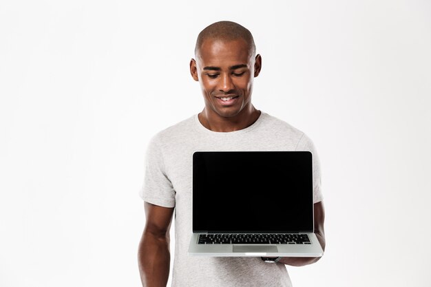 Glücklicher junger afrikanischer Mann, der Anzeige des Laptops zeigt