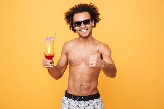 Glücklicher junger afrikanischer Mann, der Cocktail trinkt und Daumen oben zeigt.