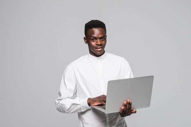 Glücklicher junger afrikanischer Mann, der lokalisiert über weißem Hintergrund unter Verwendung des Laptops steht.