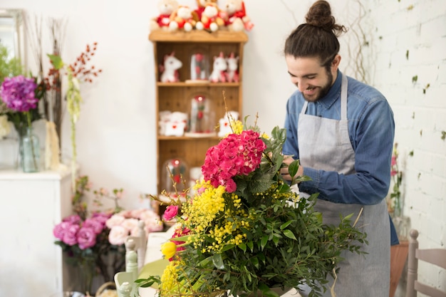 Glücklicher junger männlicher Florist, der den schönen Blumenblumenstrauß im Blumenladen schafft