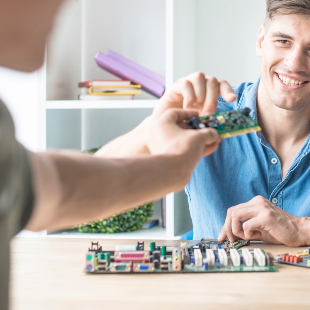 Kostenloses Foto glücklicher junger männlicher it-techniker, der hardware-stromkreis von seinem freund nimmt