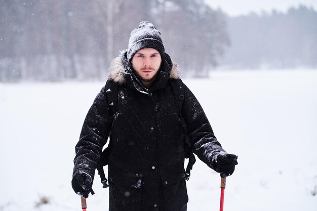 Glücklicher junger Mann beim Trekking neben einem verschneiten Wald