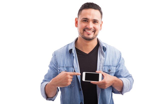 Glücklicher junger Mann, der auf den Bildschirm seines Smartphones in einem weißen Hintergrund zeigt