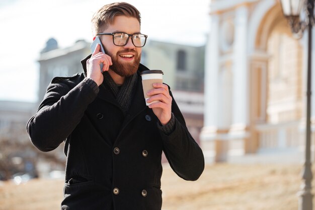 Glücklicher junger Mann, der auf Handy spricht und Kaffee trinkt