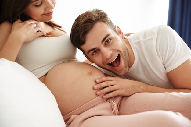 Glücklicher junger Mann, der den Bauch seiner schwangeren Frau hört