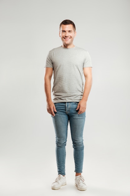 Glücklicher junger Mann gekleidet im grauen T-Shirt lokalisiert über graue Wand