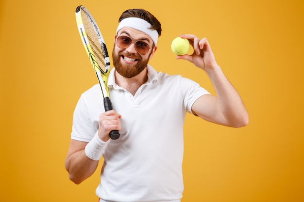 Glücklicher junger Tennisspieler, der Tennisball zeigt.