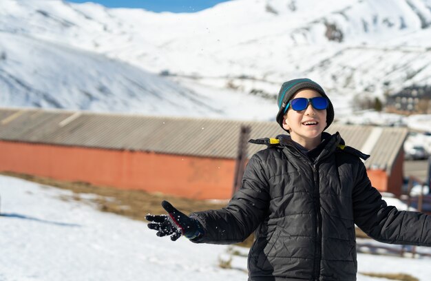 Glücklicher kaukasischer Junge, der im Winter warme Kleidung auf dem schneebedeckten Berg trägt