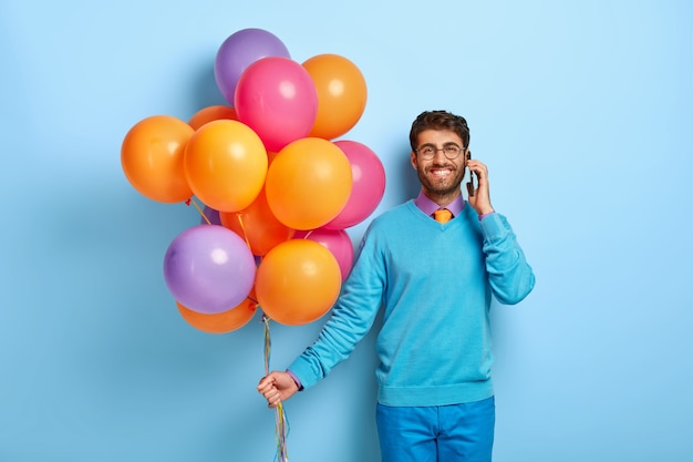 Glücklicher Kerl mit Luftballons, die im blauen Pullover aufwerfen