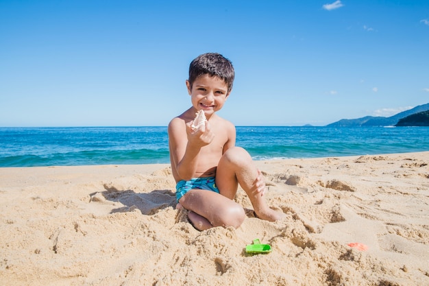 Glücklicher kleiner Junge mit Schale am Strand