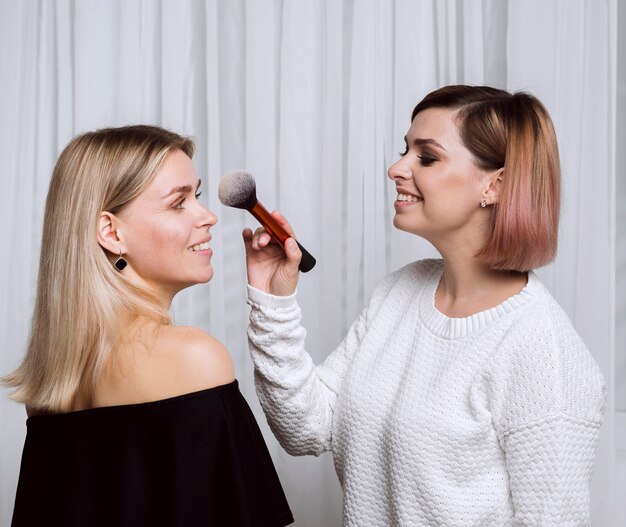 Glücklicher Künstler, der Make-up auf Modell anwendet