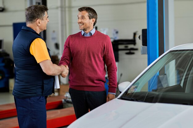 Glücklicher Kunde und Automechaniker schütteln sich die Hände, während sie in der Autowerkstatt grüßen