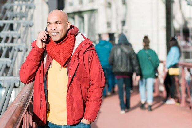 Glücklicher lächelnder hispanischer kahlköpfiger Mann mittleren Alters, der auf der Straße telefoniert