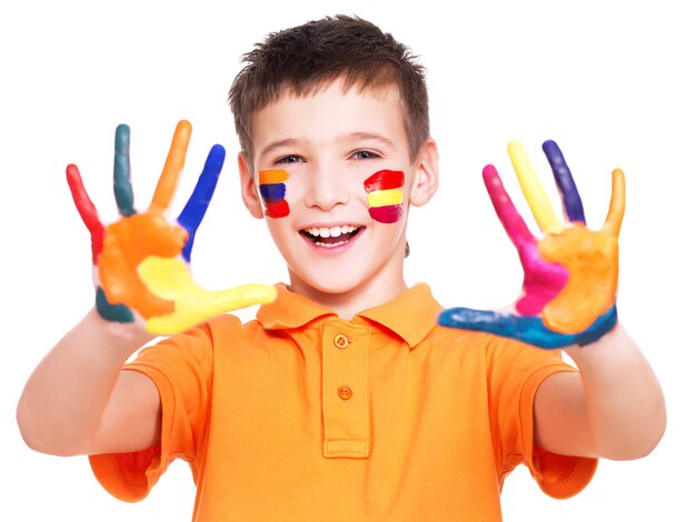 Glücklicher lächelnder Junge mit gemalten Händen und Gesicht im orange T-Shirt - auf einer weißen Wand.