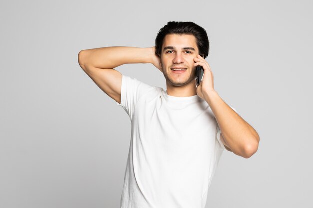 Glücklicher lächelnder junger Mann, der auf dem Handy lokalisiert auf Weiß spricht