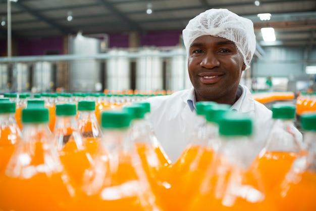 Kostenloses Foto glücklicher männlicher arbeiter, der durch orangensaftflaschen in der fabrik steht