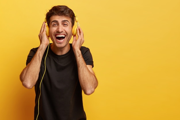 Glücklicher männlicher Meloman genießt angenehmen Klang neuer Kopfhörer, hört Lieblingsmusik