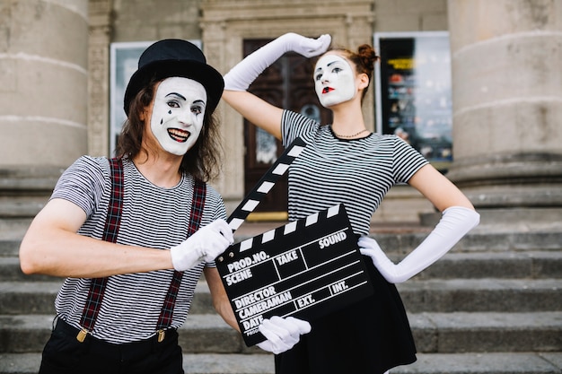 Kostenloses Foto glücklicher männlicher pantomime, der clapperboard vor der aufstellung des weiblichen pantomimen hält