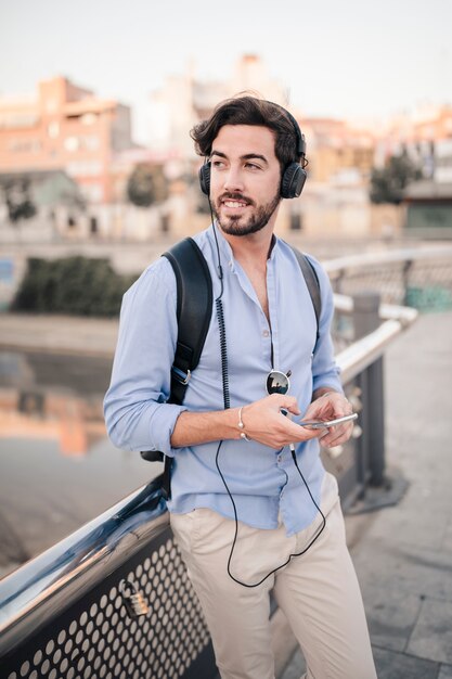 Glücklicher männlicher Tourist, der auf dem Geländer hört Musik sich lehnt