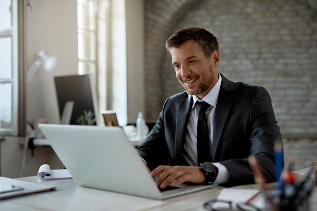 Glücklicher männlicher Unternehmer, der an einem Computer im Büro arbeitet