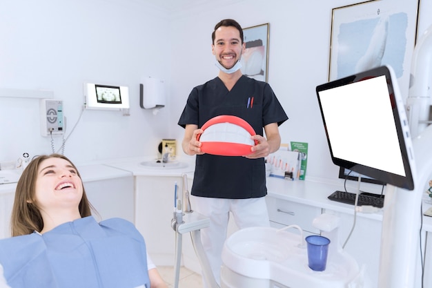 Glücklicher männlicher Zahnarzt, der großes Zahnmodell in der Klinik hält