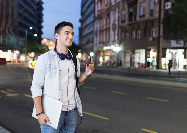 Glücklicher Mann, der auf dem Straßenrand hält Laptop steht