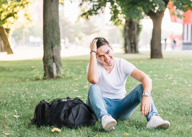 Glücklicher Mann, der auf Gras im Park sitzt