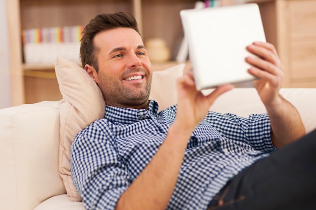 Glücklicher Mann, der auf Sofa mit digitalem Tablett entspannt