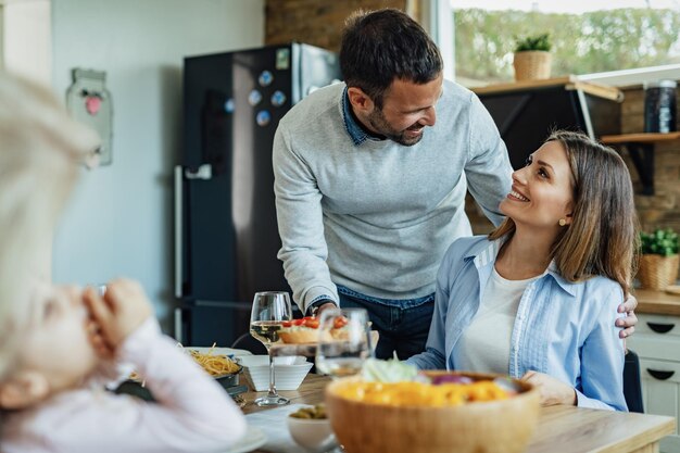 Glücklicher Mann, der Essen serviert und mit seiner Frau spricht, während er mit der Familie am Esstisch zu Mittag isst