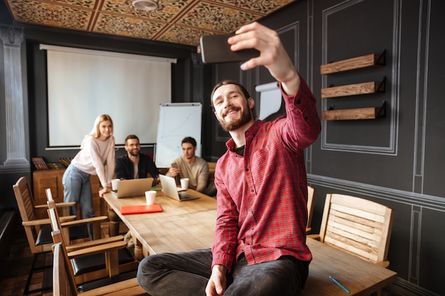 Glücklicher Mann, der im Büro sitzt und ein Selfie macht