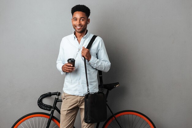 Glücklicher Mann, der nahe Fahrrad lokalisiert hört Musik, die Kaffee trinkt.