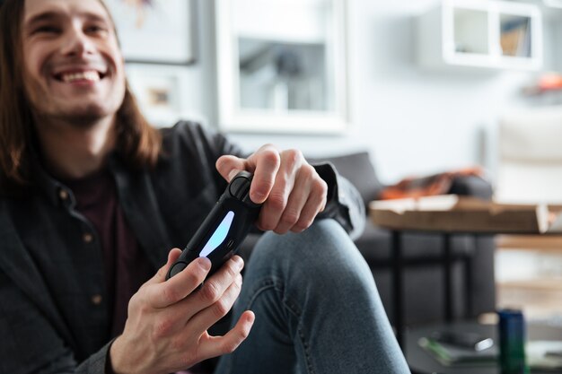 Glücklicher Mann, der zuhause drinnen sitzt, spielt mit Joystick