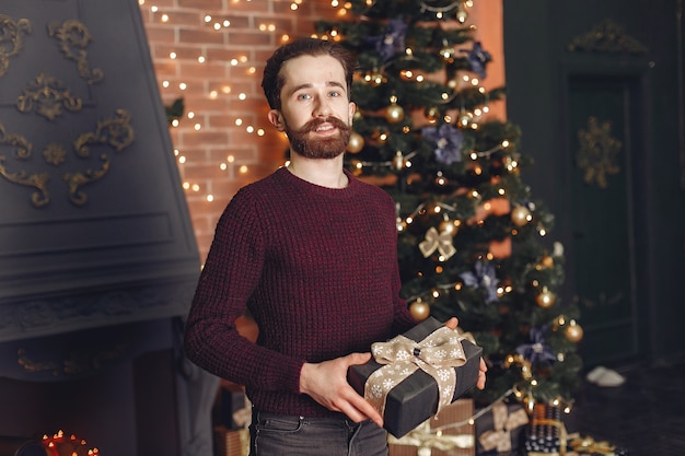 Glücklicher Mann im roten Pullover. Mann vor dem Kamin. Männchen auf dem Hintergrund des Weihnachtsbaumes.